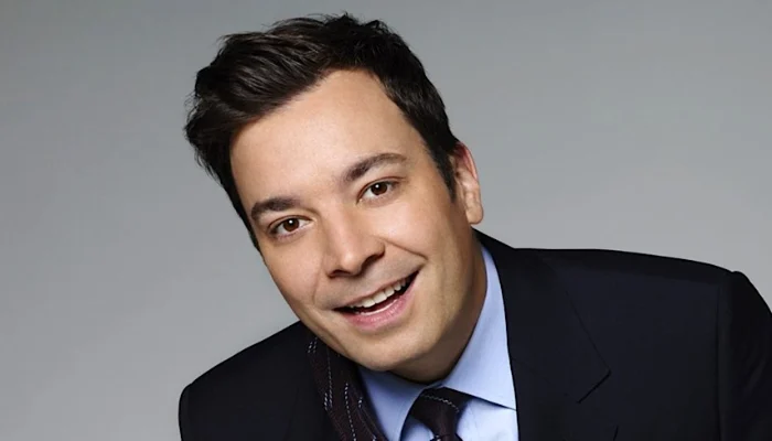 Jimmy Fallon hosting The Tonight Show with celebrity guests, performing comedy sketches, games, and viral segments in a modern late-night TV studio